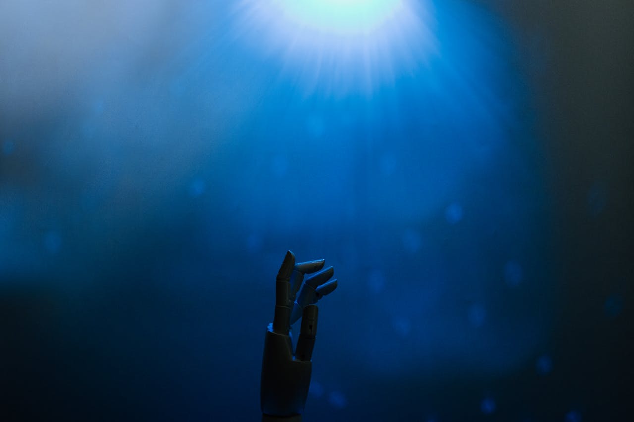 Silhouette of a robotic hand reaching towards glowing blue light in a futuristic setting.